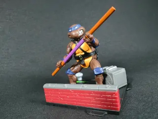 Imagen de la figura de Donatello de Las Tortugas Ninja Remastered junto con la base que forma el diorama