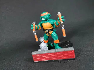 Imagen de la figura de Michelangelo de Las Tortugas Ninja Remastered junto con la base que forma el diorama