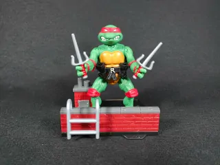 Imagen de la figura de Raphael de Las Tortugas Ninja Remastered junto con la base que forma el diorama