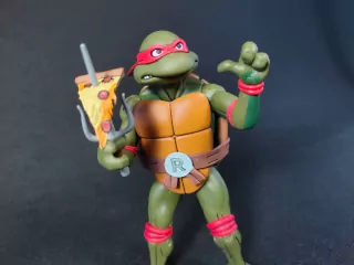 Imagen de la figura de Raphael Cartoon con sus sais y el trozo de pizza